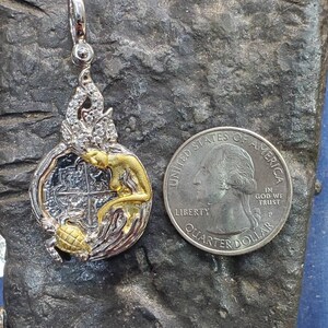 May include: Silver and gold pendant featuring a mermaid with a treasure map inside a circle. The pendant is about the size of a US quarter.