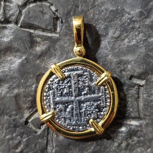 Pu&ograve; includere: Un ciondolo d'oro con una moneta d'argento che presenta una croce e disegni intricati. La moneta &egrave; circondata da una cornice d'oro con quattro accenti decorativi.
