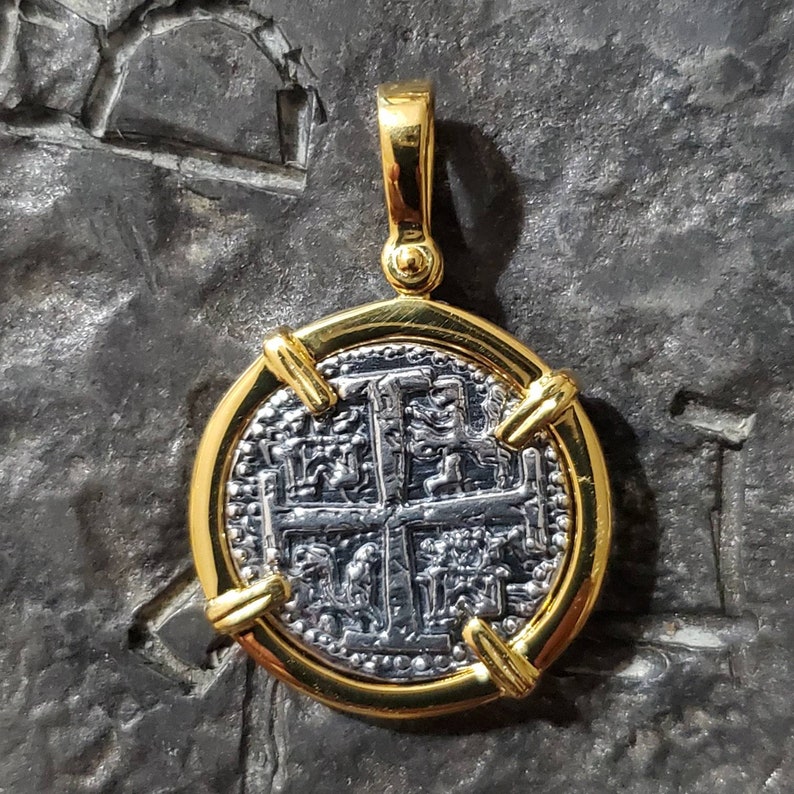 Pu&ograve; includere: Un ciondolo d'oro con una moneta d'argento che presenta una croce e disegni intricati. La moneta &egrave; circondata da una cornice d'oro con quattro accenti decorativi.