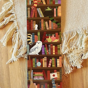 May include: A brown wooden bookshelf filled with colorful books, a white owl perched on a shelf, a green cauldron, a broom, and a red envelope with a wax seal.