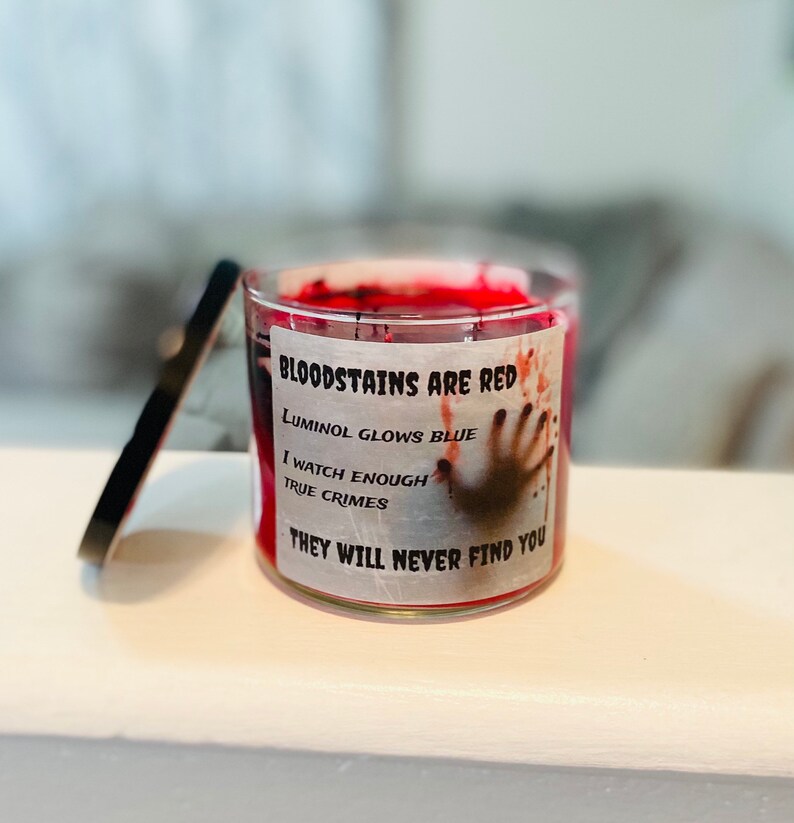 May include: A red candle with a white label that reads "BLOODSTAINS ARE RED, LUMINOL GLOWS BLUE, I WATCH ENOUGH TRUE CRIMES, THEY WILL NEVER FIND YOU". The label also features a bloody handprint.