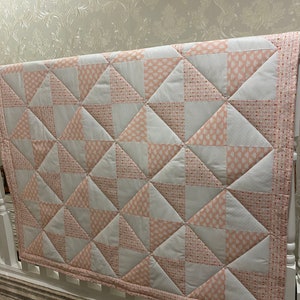 May include: A pink and white patchwork quilt with a geometric pattern. The quilt is made of squares and triangles and has a white border.