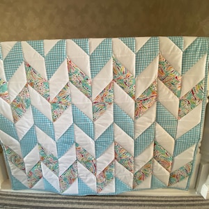 May include: A blue and white chevron patterned quilt with a white background and blue gingham accents.