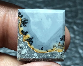 以下が含まれることがあります： 黒と黄色の樹枝状模様が入った、正方形の灰色のアゲートカボション。アゲートは、ざらざらとした質感の表面をしています。