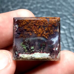 May include: A square-shaped agate gemstone with a layered pattern of brown, white, and green dendrites. The agate is translucent, allowing light to pass through it.