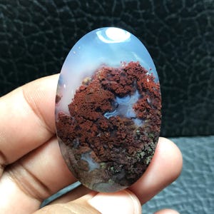 Peut inclure: Cabochon d'agate de forme ovale avec un fond blanc et des motifs dendritiques rouges, bruns et verts.