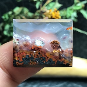May include: A clear agate cabochon with a layered pattern of white, brown, and orange. The agate has a cloudy, translucent appearance.