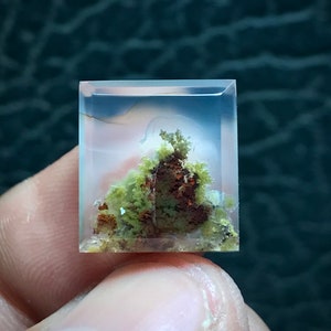 May include: A clear quartz crystal with inclusions of green and brown minerals. The crystal is cut into a square shape and has a polished finish.