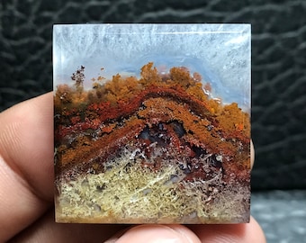 Può includere: Un cabochon quadrato di quarzo trasparente con un motivo di agata a strati. L'agata presenta uno schema di colori marrone, rosso e bianco con un motivo dendritico.