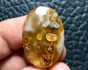 Pode incluir: Um cabochão de ágata marrom e branco com um padrão único de redemoinhos e manchas marrons e brancas. A pedra tem formato oval e uma superfície lisa e polida.