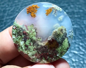 May include: A round, white agate geode with a landscape-like pattern of green, brown, and orange dendrites. The geode is polished and smooth.