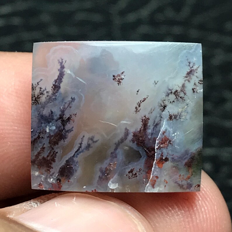 May include: Square-cut gemstone with a dendritic pattern. The stone features a cloudy, light background with dark brown and reddish-brown fern-like inclusions. The overall effect resembles a miniature landscape.