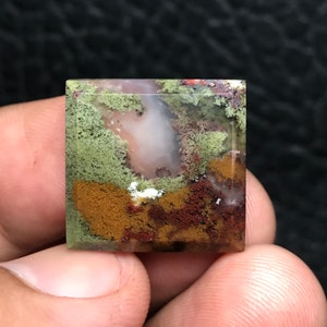 Peut inclure: Un cabochon d'agate de forme carrée, translucide, vert, brun et blanc, avec une surface polie. La pierre présente un motif unique et stratifié avec des nuances de vert, de brun et de blanc.