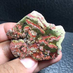 May include: A close-up of a green and red agate stone with a swirling pattern. The stone is smooth and polished, and it has a natural, organic look.