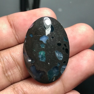 Puede incluir: Piedra preciosa ovalada en cabujón con base negra e inclusiones de ópalo azul, verde y blanco.