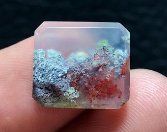 Op de afbeelding: Een vierkante, doorschijnende, roze agaat edelsteen met een dendritisch patroon van groene, blauwe en rode insluitsels. De agaat is geslepen en gepolijst.
