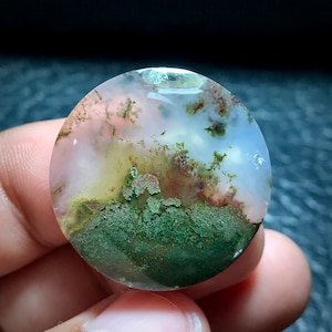 May include: A round, polished agate cabochon with a pink, white, and green colour pattern. The stone has a unique, mossy appearance.