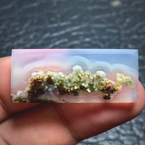 May include: A rectangular polished gemstone cabochon featuring a translucent, milky white and pale blue base with internal moss-like inclusions in shades of deep brown, olive green, and cream, creating a landscape-like pattern within the stone.