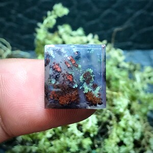 May include: A square-shaped, translucent agate cabochon with a unique pattern of brown, red, and green inclusions. The agate has a polished surface and is a natural gemstone.
