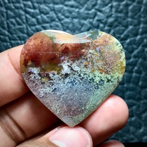 May include: A heart-shaped agate stone with a unique pattern of red, brown, green, and white. The stone has a smooth, polished surface.