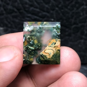 Könnte beinhalten: Ein grüner, brauner und weißer Achat-Cabochon mit polierter, rechteckiger Form. Der Stein hat eine trübe, durchscheinende Optik mit Farbwirbeln.