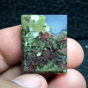 Könnte beinhalten: Ein grüner, weißer und brauner Achat-Cabochon mit einem einzigartigen Landschaftsmuster. Der Stein ist in rechteckiger Form geschnitten und hat eine glatte, polierte Oberfläche.