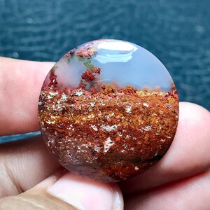 May include: A round, polished agate cabochon with a white, cloudy center and a layered, brown, red, and orange base.