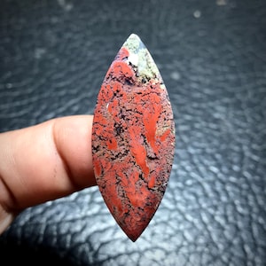 Könnte beinhalten: Ein roter, weißer und schwarzer Achat-Cabochon mit einem einzigartigen, marmorierten Muster. Der Cabochon ist tropfenförmig und hat eine glatte, polierte Oberfläche.