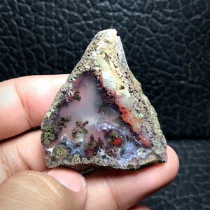 May include: A triangular piece of agate with a variety of colours, including white, pink, red, and green. The agate has a dendritic pattern and is translucent.