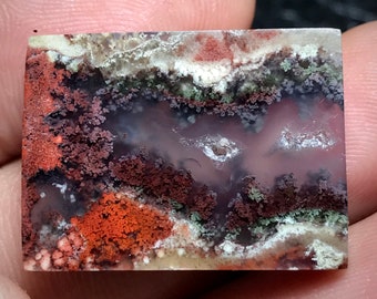 Pode incluir: Uma pedra de ágata polida com uma variedade de cores e padrões, incluindo vermelho, marrom, branco e verde. A pedra tem uma aparência em camadas, com diferentes cores e padrões sobrepostos.