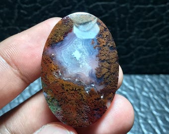 May include: A polished oval cabochon of agate with a white and pink center surrounded by brown, orange, and green dendrites.