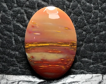 May include: Oval shaped cabochon gemstone with a red, orange, and yellow color pattern. The stone has a polished, smooth surface and a layered, banded appearance.