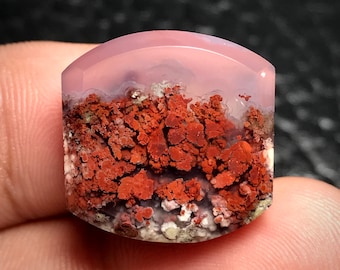 May include: A pink and red agate cabochon with a unique pattern of red and white inclusions. The agate is polished and has a smooth, rounded surface.