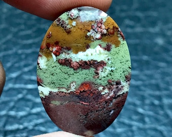 Op de afbeelding: Ovale cabochon van groene, bruine, oranje en witte agaat met een gelaagd, landschapsachtig patroon.