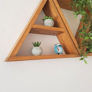 Peut inclure: Une &eacute;tag&egrave;re triangulaire en bois avec trois tablettes. Les tablettes sont d&eacute;cor&eacute;es de petites plantes en pot et d'un r&eacute;veil bleu.