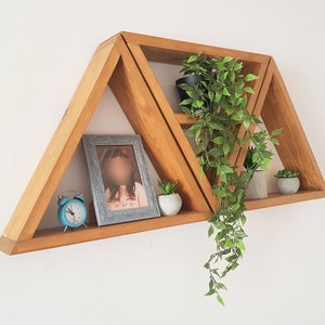 Peut inclure: Un ensemble de trois &eacute;tag&egrave;res triangulaires en bois avec un cadre photo, une horloge et des plantes en pot. Les &eacute;tag&egrave;res sont fix&eacute;es &agrave; un mur blanc.