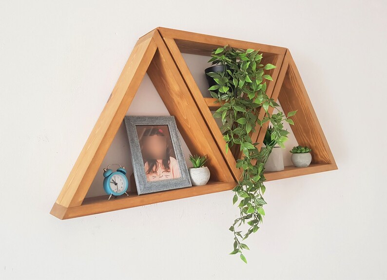 Peut inclure: Un ensemble de trois &eacute;tag&egrave;res triangulaires en bois avec un cadre photo, une horloge et des plantes en pot. Les &eacute;tag&egrave;res sont fix&eacute;es &agrave; un mur blanc.