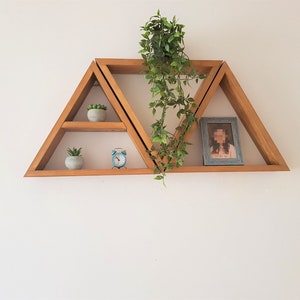 Peut inclure: Un ensemble de trois &eacute;tag&egrave;res triangulaires en bois fix&eacute;es &agrave; un mur blanc. Les &eacute;tag&egrave;res sont d&eacute;cor&eacute;es de petites plantes en pot et d'une photo encadr&eacute;e.