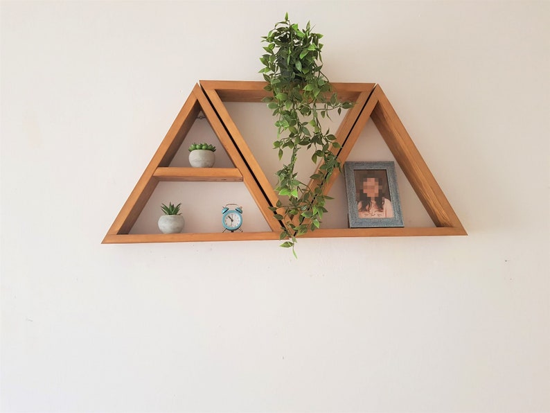 Peut inclure: Un ensemble de trois &eacute;tag&egrave;res triangulaires en bois fix&eacute;es &agrave; un mur blanc. Les &eacute;tag&egrave;res sont d&eacute;cor&eacute;es de petites plantes en pot et d'une photo encadr&eacute;e.