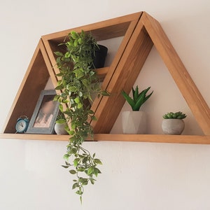 Peut inclure: Une &eacute;tag&egrave;re en bois triangulaire avec trois tablettes. Les tablettes sont d&eacute;cor&eacute;es de plantes en pot, d'un cadre photo et d'une petite horloge.