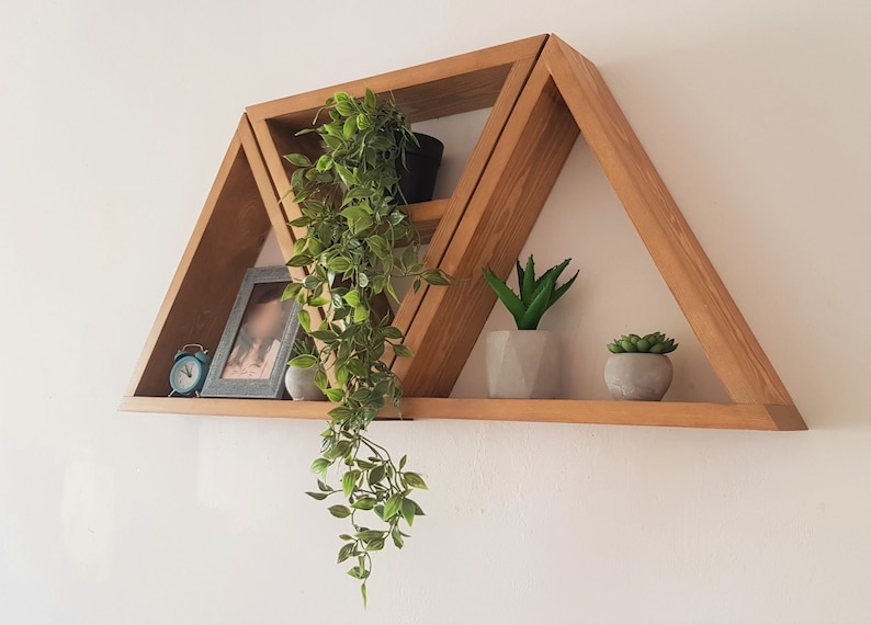 Peut inclure: Une &eacute;tag&egrave;re en bois triangulaire avec trois tablettes. Les tablettes sont d&eacute;cor&eacute;es de plantes en pot, d'un cadre photo et d'une petite horloge.