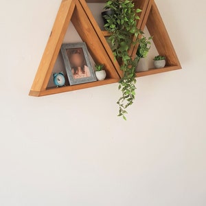 Peut inclure: Un ensemble de trois &eacute;tag&egrave;res triangulaires en bois fix&eacute;es &agrave; un mur blanc. Les &eacute;tag&egrave;res sont dispos&eacute;es en quinconce, la plus haute &eacute;tant la plus petite et la plus basse la plus grande. Les &eacute;tag&egrave;res sont d&eacute;cor&eacute;es d'une petite horloge, d'une photo encadr&eacute;e et de deux plantes en pot.