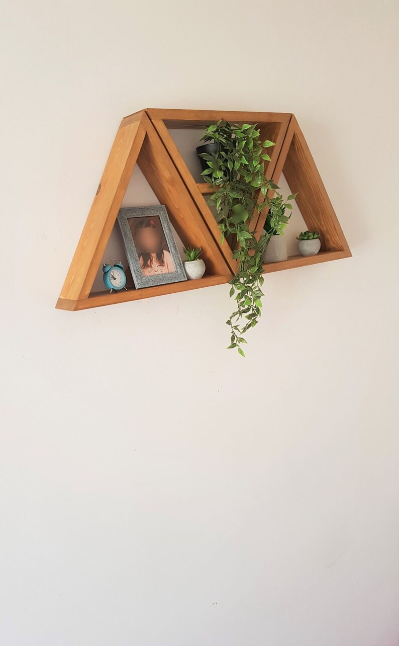 Peut inclure: Un ensemble de trois &eacute;tag&egrave;res triangulaires en bois fix&eacute;es &agrave; un mur blanc. Les &eacute;tag&egrave;res sont dispos&eacute;es en quinconce, la plus haute &eacute;tant la plus petite et la plus basse la plus grande. Les &eacute;tag&egrave;res sont d&eacute;cor&eacute;es d'une petite horloge, d'une photo encadr&eacute;e et de deux plantes en pot.