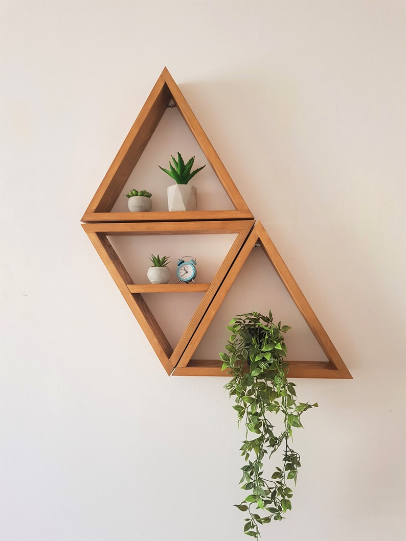 Peut inclure: Trois &eacute;tag&egrave;res triangulaires en bois mont&eacute;es sur un mur blanc. L'&eacute;tag&egrave;re du haut a deux petites plantes en pot, l'&eacute;tag&egrave;re du milieu a une petite plante en pot et un r&eacute;veil bleu, et l'&eacute;tag&egrave;re du bas a une plante suspendue avec des feuilles vertes.