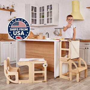 May include: A wooden learning tower and a small wooden desk with a chair are in a kitchen. The learning tower has a canvas panel. A child is standing in the learning tower. The kitchen has white cabinets and wooden shelves.