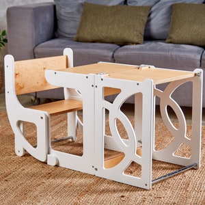 May include: White wooden children's table and chair set with a natural wood top. The table has a unique design with cutouts and the chair has a back and a seat.