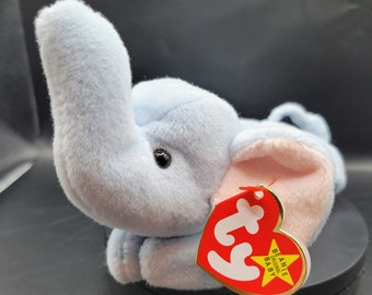 May include: A light blue plush elephant with a pink ear and a red Ty Beanie Baby tag. The tag has a white star and the words "Beanie Original Baby" on it.