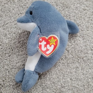 May include: A blue and white Ty Beanie Baby dolphin plush toy with a red tag that says "Beanie Babies Original Baby ty".