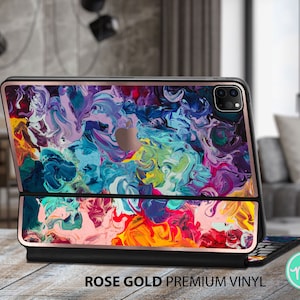 May include: Rose gold iPad case with a vibrant abstract art design in shades of blue, purple, yellow, and pink. The case is shown with a black keyboard attached. The text "ROSE GOLD PREMIUM VINYL" is displayed at the bottom.