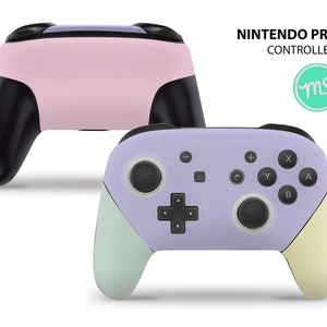 Könnte beinhalten: Zwei Nintendo Pro-Controller, einer in Pink und einer in Lila mit einem hellgrünen und gelben Akzent. Die Controller werden vor einem weißen Hintergrund gezeigt.